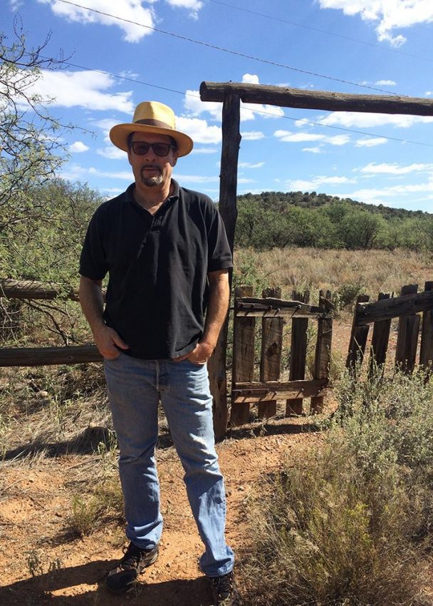 Man wearing a hat standing next to a wooden fence.