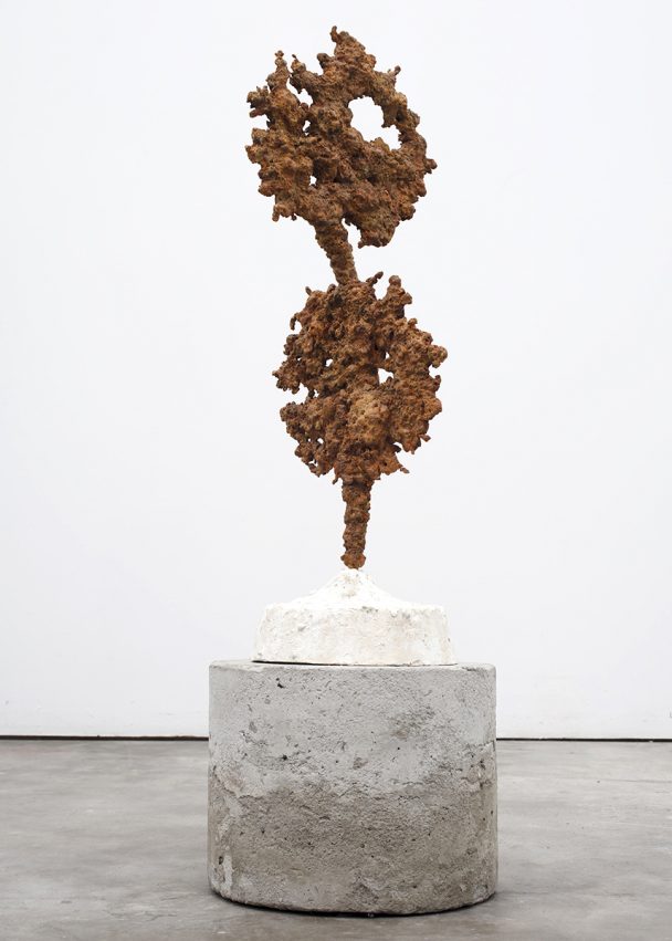 A rusty metal sculpture on a concrete pedestal.