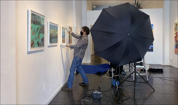 A man hanging paintings in an art gallery.