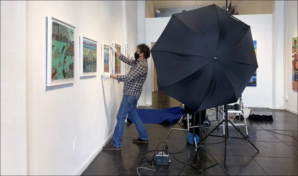 A man hanging paintings in an art gallery.