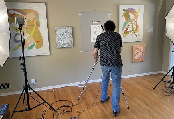 Man photographing abstract paintings in a room.