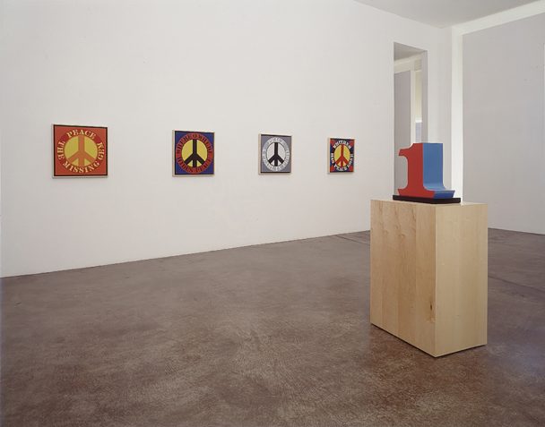 Four peace symbol paintings and a blue number one sculpture.